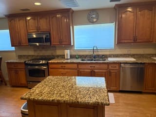 Fully equipped kitchen with granite island, stainless steel appliances, wooden cabinetry, and tile backsplash